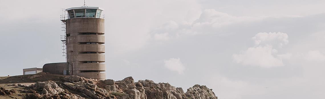 Photo of cliff headland with old german radio tower, sea in background with patchy sun and clouds